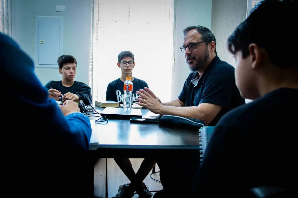 Tutor conversa com estudantes ao redor da mesa durante um encontro da Mentoria